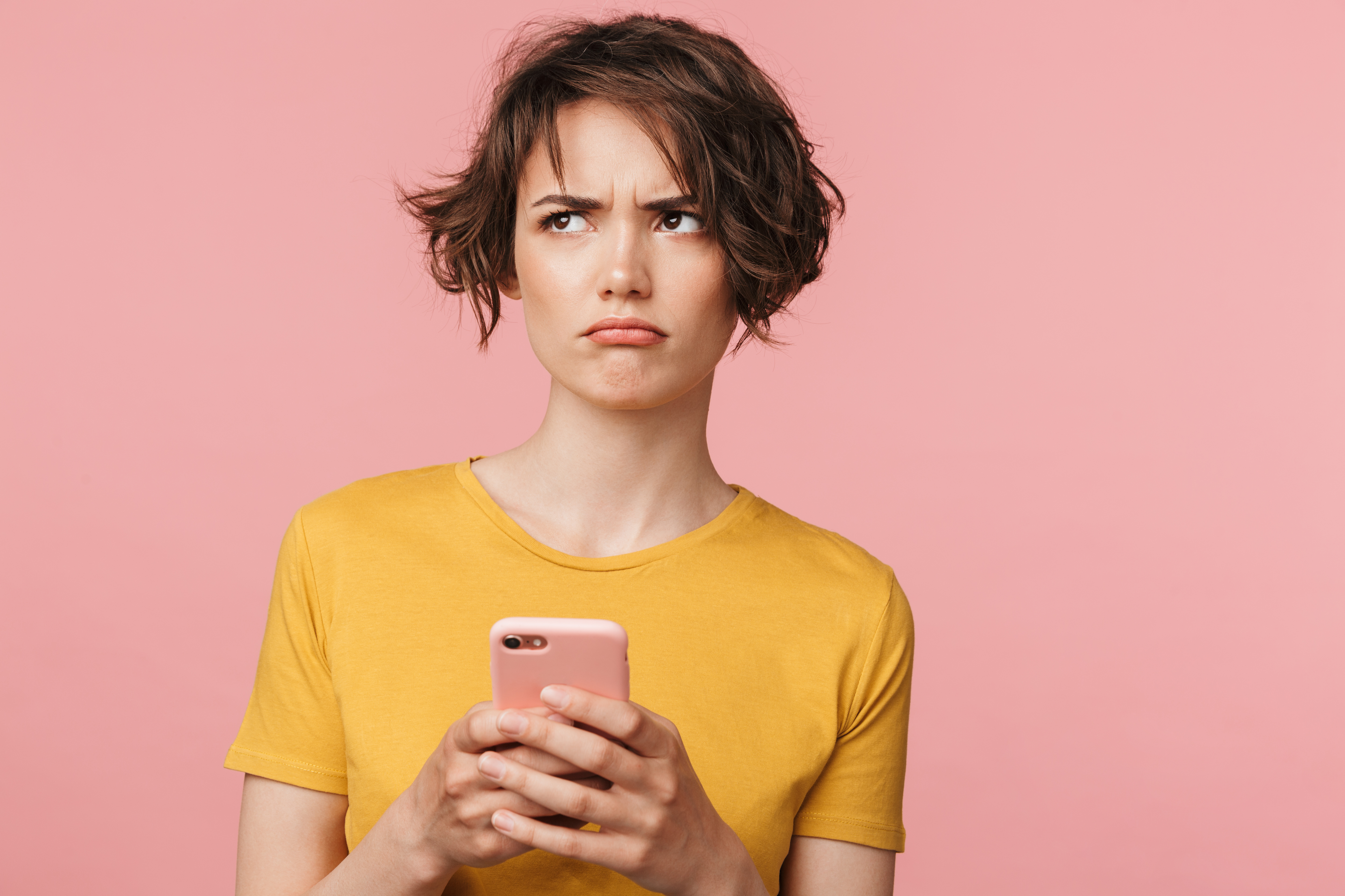 A brunette woman in a yellow shirt holding a mobile phone