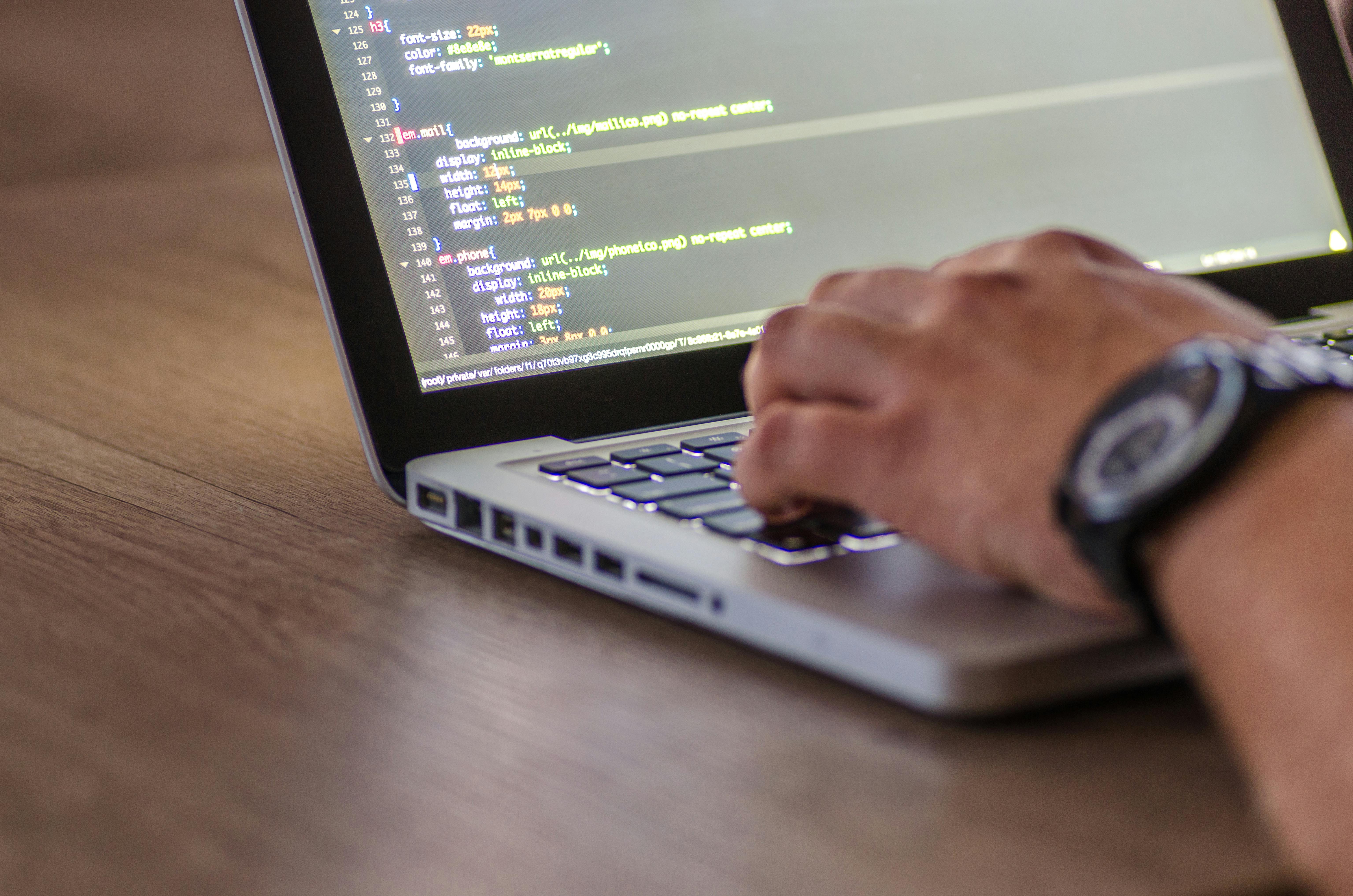 laptop with code on its screen and hands typing